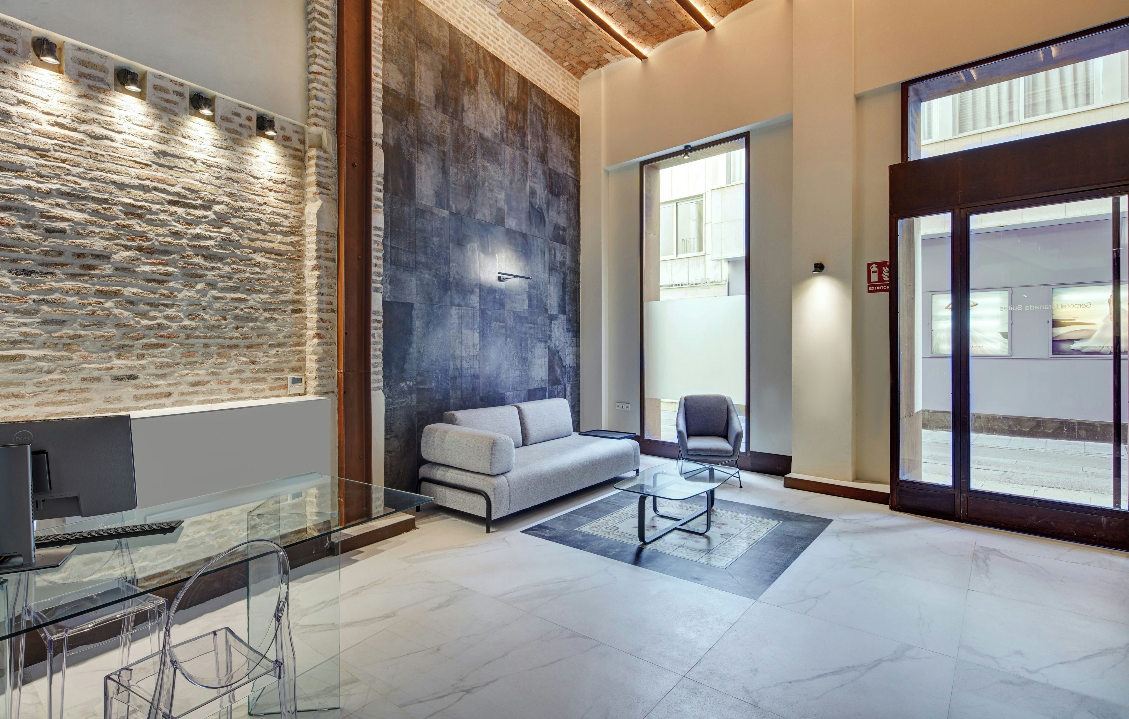 A modern interior with a stone wall, a grey sofa, a glass table, and a clear desk area.