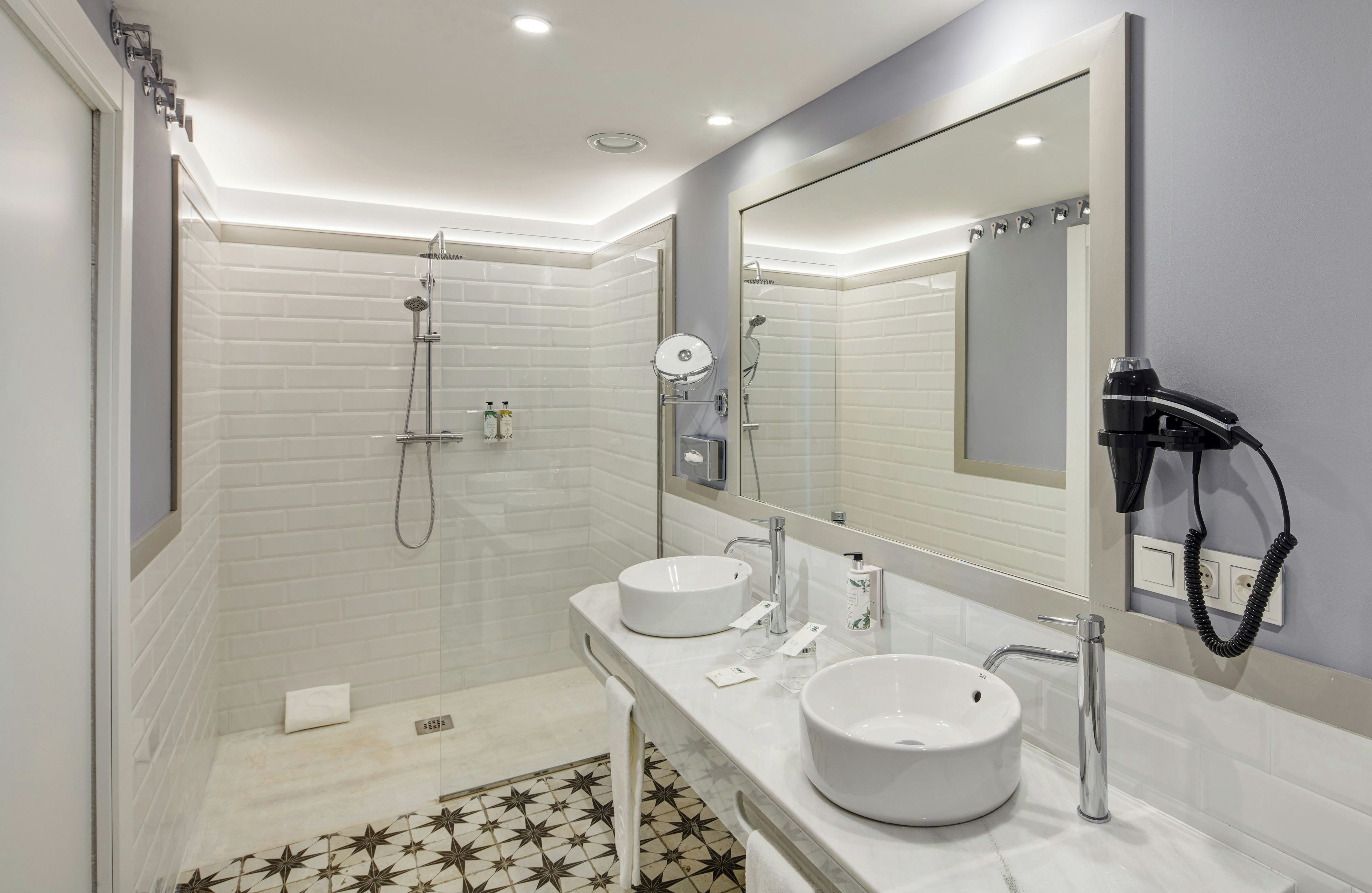 Une salle de bain moderne avec deux lavabos, une douche et un sèche-cheveux fixé au mur.