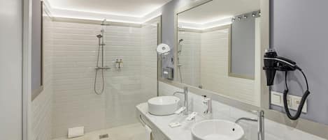 A modern bathroom with two sinks, a shower, and a hairdryer mounted on the wall.