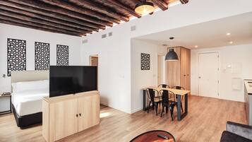 Ett modernt hotellrum med ett träpanelat tak, en platt-TV, en säng, en matplats med bord och stolar samt dekorativa väggpaneler.