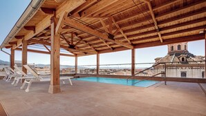 Una piscina en la azotea con vigas de madera y sillones de descanso.