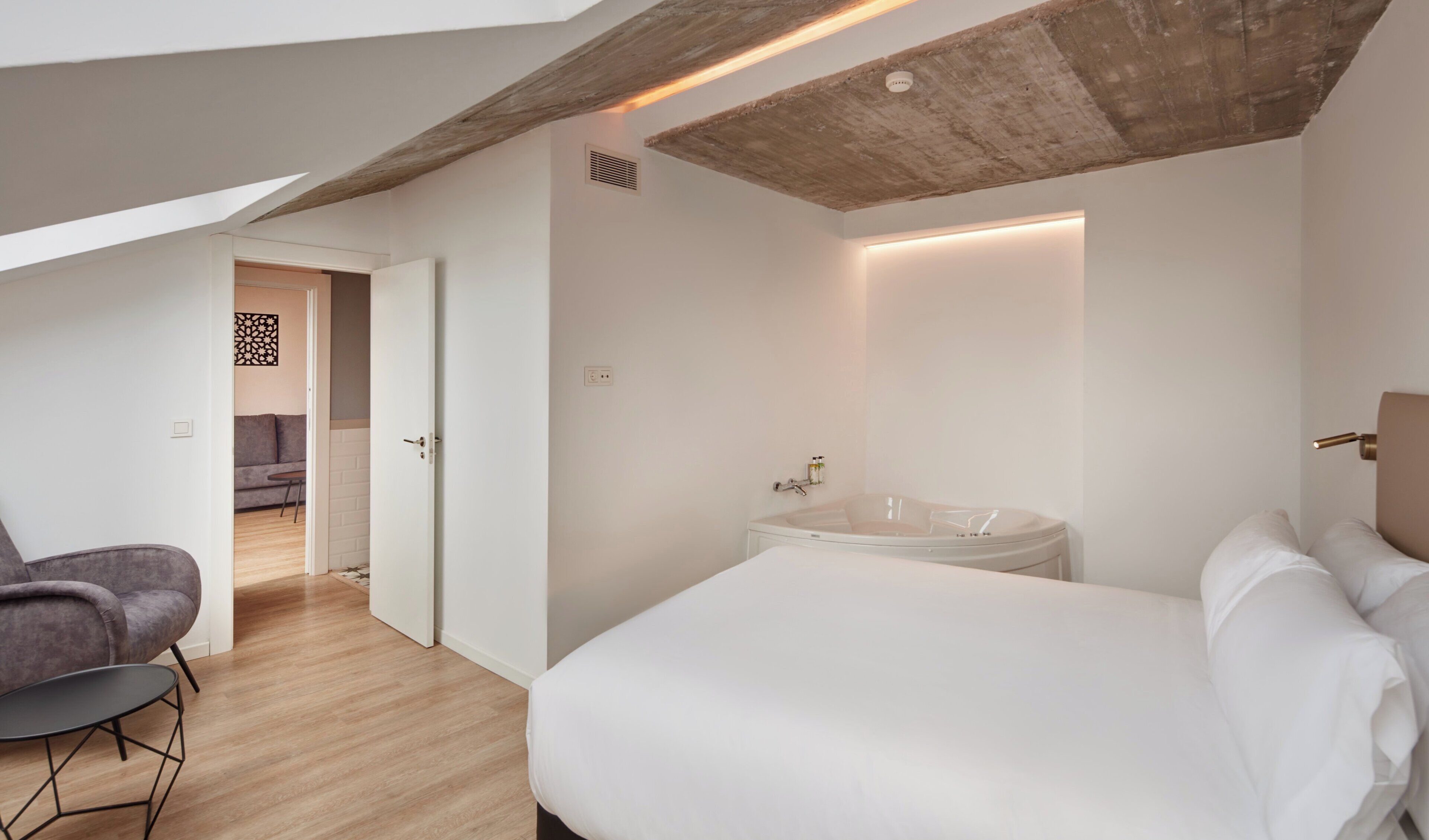 A modern bedroom with a large bed, a built-in bathtub, and a seating area with a chair.