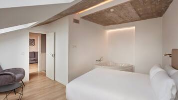 A modern bedroom with a large bed, a built-in bathtub, and a seating area with a chair.