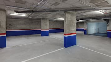 Un aparcamiento con pilares de hormigón, paredes pintadas de azul y rojo, e iluminación fluorescente.