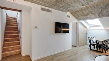 Un interior moderno con una escalera de madera, un televisor de pantalla plana montado en la pared y un tragaluz sobre una zona de comedor.