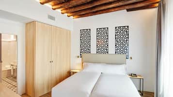A hotel room with a wooden wardrobe, a bed with white bedding, decorative wall panels, and a bedside table with a lamp.