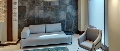 A modern interior with a stone wall, a sofa, a chair, and a patterned rug.