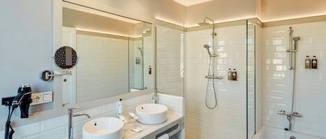 A modern bathroom with two sinks, a large mirror, a hairdryer, and a glass-enclosed shower area.