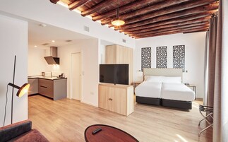 Une chambre d’hôtel moderne avec un plafond en bois, un téléviseur à écran plat, un lit avec une literie blanche, un bureau avec un ordinateur et un coin repas.