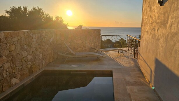 A stone wall, a pool, and a view of the sea at sunset.