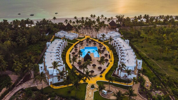 An aerial view of a resort with a central pool, surrounded by white buildings and palm trees, overlooking a beach and ocean. - SBH Kilindini Resort (Matemwe)