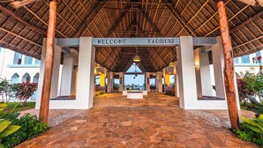 A welcoming entrance with a thatched roof and a 'Welcome Karibuni' sign, leading to a spacious area with stone flooring and potted plants. - SBH Kilindini Resort (Matemwe)