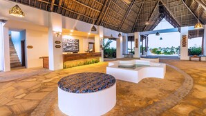 A spacious lobby with a high ceiling, a reception desk, and a seating area with a stone-tiled circular bench. - SBH Kilindini Resort (Matemwe)