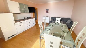 A modern kitchen with white cabinets and a dining area with a glass table and white chairs. - Holiday apartment with balcony, WiFi and air conditioning (Novi Vinodolski)