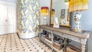Un couloir avec un papier peint à motifs, un miroir, une lampe et une étagère décorative.