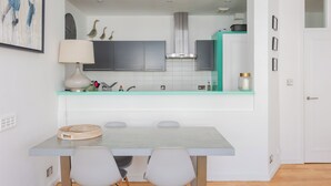 Une cuisine moderne avec des meubles gris, un plan de travail de couleur turquoise et un coin repas comprenant une table et des chaises.
