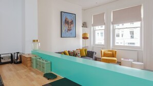 Un salon moderne avec un mur d’accent de couleur turquoise, un canapé agrémenté de coussins colorés, un fauteuil jaune, une table basse et une grande fenêtre avec des stores.