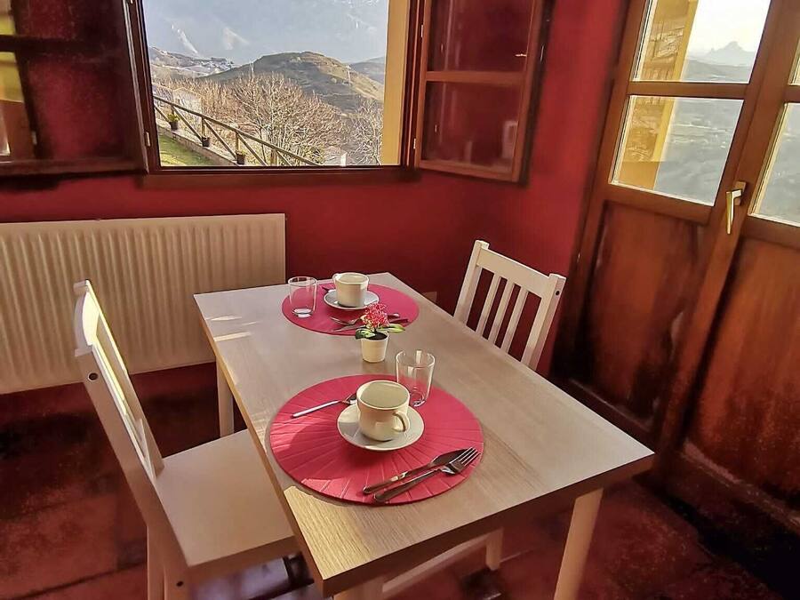 Ein Essbereich mit Tisch für zwei Personen, Blick auf Berge durch ein Fenster und einer roten Wand.