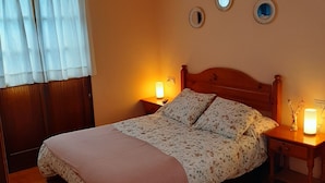 Quarto com cama de madeira, duas luminárias laterais, ventoinha no teto e janela com cortinas.