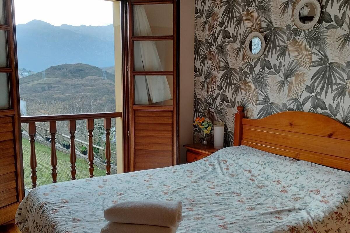 A bedroom with a wooden bed, floral bedspread, and a view of mountains through a balcony.