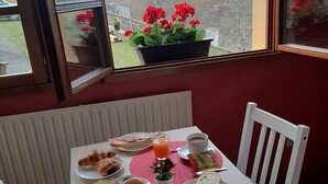 Mesa de café da manhã com croissants, pão, cereais, café e suco, com vista para as montanhas.