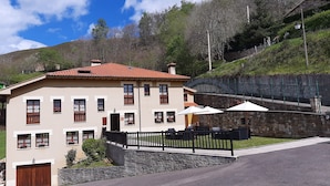 Um edifício de dois andares com telhado de telhas vermelhas, parede de pedra e área de estar externa com guarda-sóis.