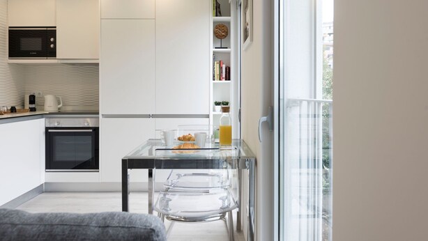 Una cocina moderna con un microondas Bosch, una cafetera y una mesa de vidrio con alimentos para el desayuno.