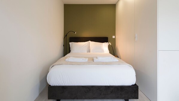 A neatly made bed with white linens and towels, a dark headboard, and a lamp on the nightstand.