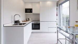 Una cocina moderna con armarios blancos, un lavamanos de acero inoxidable, un horno empotrado y un microondas.