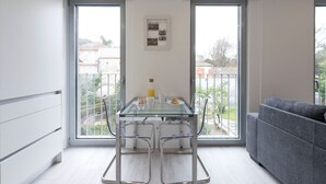 Un apartamento moderno con una mesa de comedor de vidrio, un sofá gris y un balcón con vistas a la ciudad.