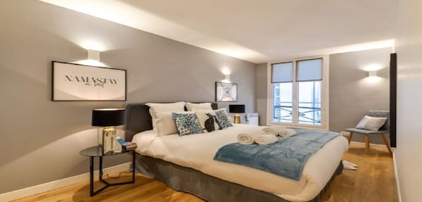 A modern bedroom with a large bed, bedside tables, a window with a view, and a framed artwork on the wall.