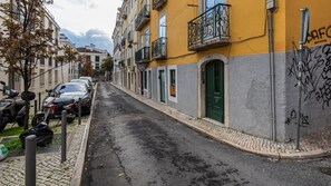 Eine schmale Straße gesäumt von parkenden Autos und einem Gebäude mit grüner Tür und Balkonen.
