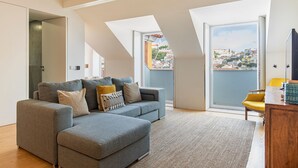 Uma sala de estar moderna com um sofá seccional cinza, um armário de madeira e vista para a paisagem urbana através de grandes janelas.