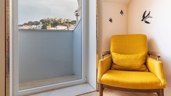 Ein Zimmer mit gelbem Ohrensessel, einem Fenster mit Blick auf eine historische Stadtansicht und Wandgestaltung.