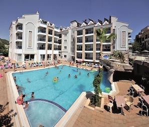 A hotel with a large pool surrounded by lounge chairs and umbrellas, multiple balconies, and a tropical-themed poolside area. - Epic Hotel (Marmaris)