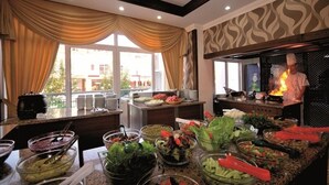Ein reichhaltiges Buffet mit verschiedenen Speisen, ein Koch am Werk und Blick ins Freie.