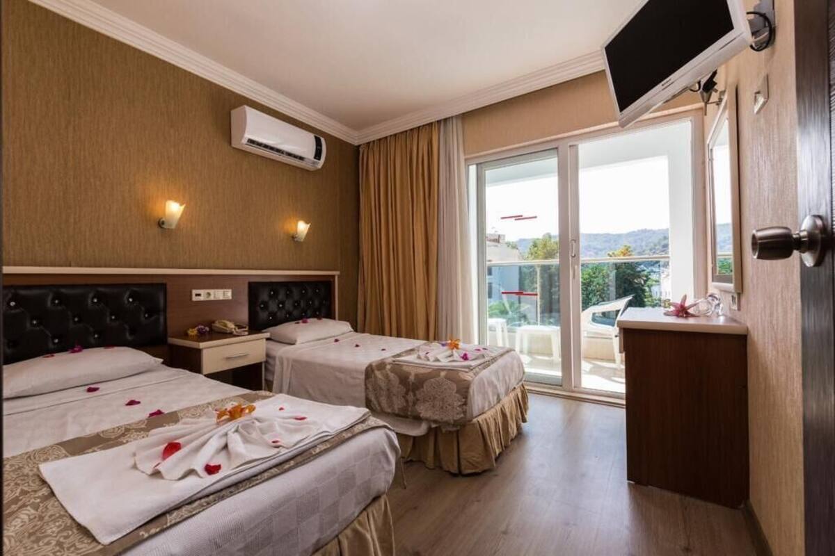 A hotel room with two beds, a TV, a desk, and a balcony with a view.
