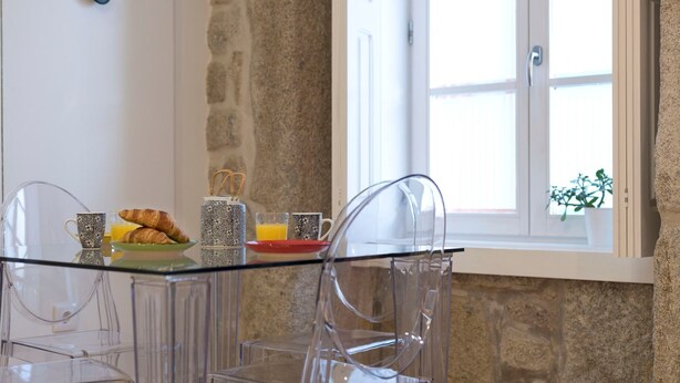 A breakfast setup with croissants, orange juice, and coffee on a glass table in a room with stone walls and a window. - Modern Vitoria Getaway by LovelyStay (Porto)