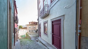 A narrow cobblestone alley with buildings on either side, featuring a red door and a balcony with ornate metal railings. - Modern Vitoria Getaway by LovelyStay (Porto)