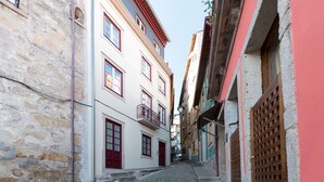 A narrow cobblestone street flanked by historic buildings with balconies and red doors. - Modern Vitoria Getaway by LovelyStay (Porto)