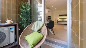 A modern living room with a wicker chair, a table with a kettle, and a large potted plant.