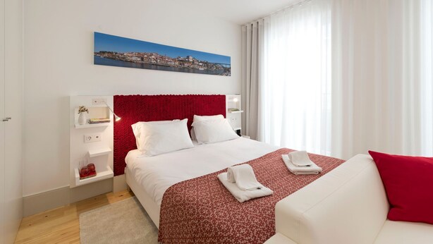 Een hotelkamer met een bed, een rood hoofdeinde, een witte bank en een stadsgezichtschilderij aan de muur.