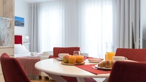 Hotelkamer met een eethoek, bestaande uit een ronde tafel, rode stoelen en ontbijtartikelen zoals fruit, een croissant en sinaasappelsap.