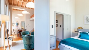 A modern bedroom with a bed, a desk, and a chair. There is a hallway leading to another room.
