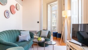A living room with a green sofa, a small round table with a glass of wine and grapes, a floor lamp, and a TV. - Luxurious Duplex with Unique View by LovelyStay (Porto)