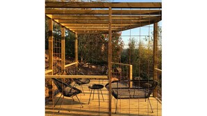 Un espacio de estar al aire libre cubierto, con sillas de metal y una estructura de pérgola de madera.