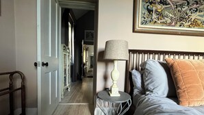 A bedroom with a bed, a bedside table with a lamp, a wooden floor, and a door leading to a hallway. - Easel Cottage near Wells: an art-filled hideaway adjacent to Andelli Art gallery (Wells)