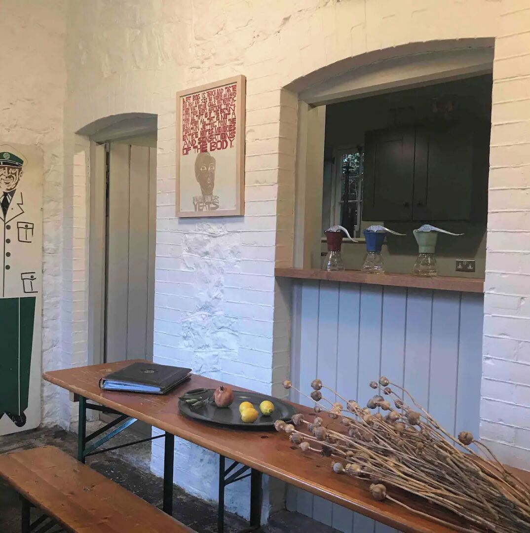 Una habitación con una mesa de madera, un banco, un cartel enmarco y una ventana con vistas.