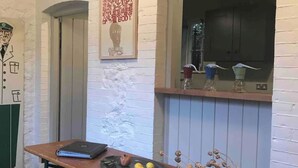 A room with a wooden table, a bench, a framed poster, and a window with a view. - Easel Cottage near Wells: an art-filled hideaway adjacent to Andelli Art gallery (Wells)