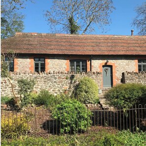 Traditional stone building with a sloped red-tiled roof and a green door.
